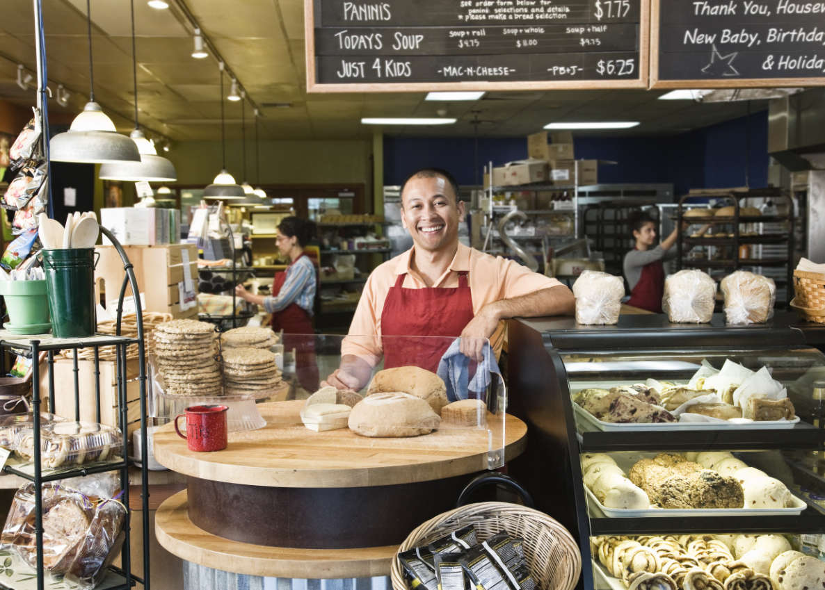 Hispanic man baker and employees in the backgrtound of the bakery. Divi Magic Bakery theme layout for WordPress